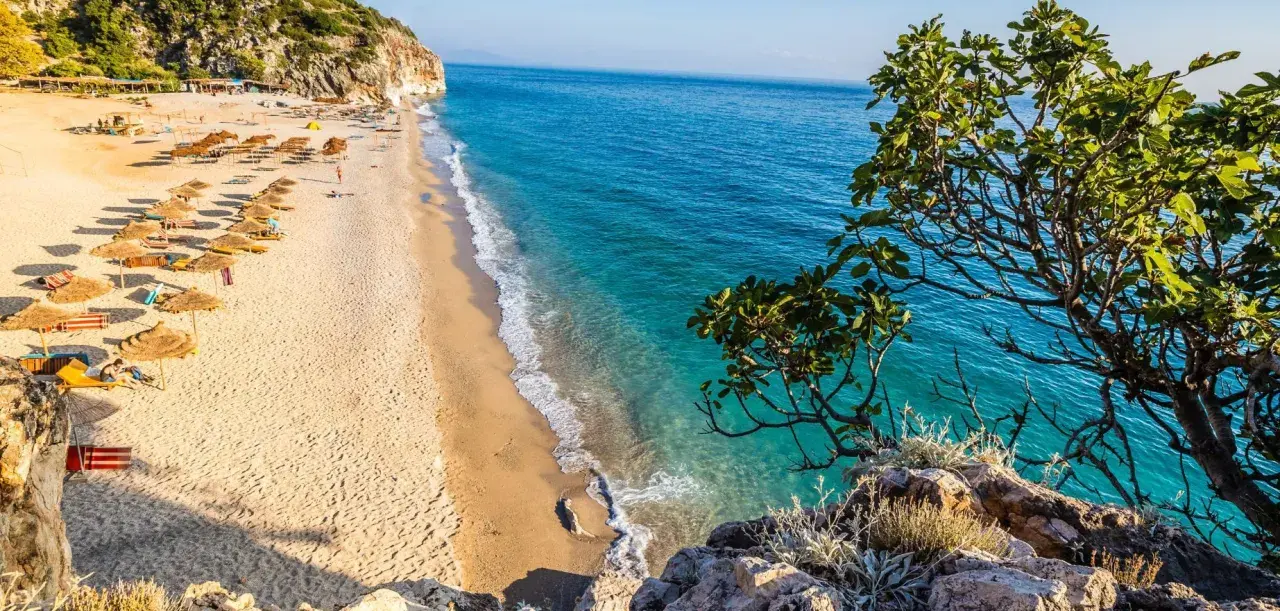 Piękna plaża w Albanii z turkusową wodą i rzędami parasoli. Ceny wakacji w Albanii są przystępne, a widoki zachwycające.