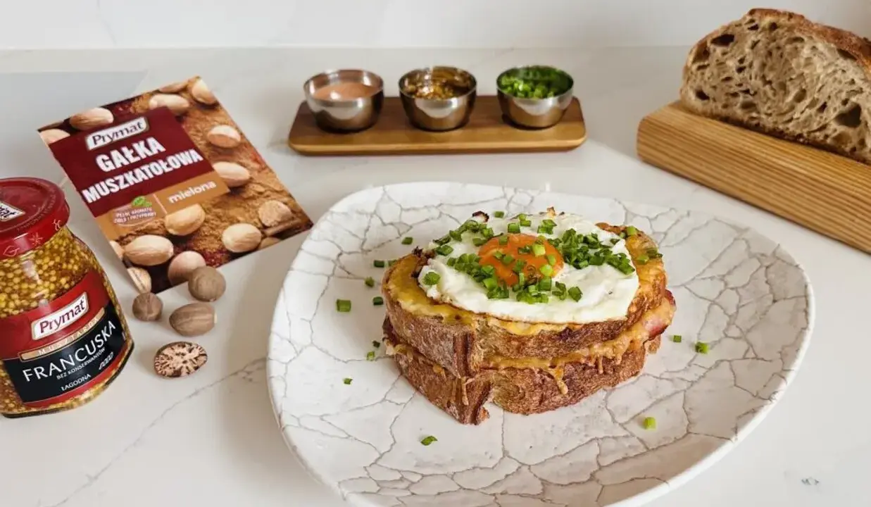 Pyszny croque madame z jajkiem sadzonym i szczypiorkiem, obok musztarda francuska i gałka muszkatołowa.