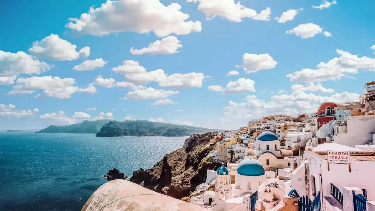 Santorini, Grecja. Białe domy z niebieskimi kopułami kościołów na zboczu góry, widok na morze. Zastanawiasz się, ile się leci do Grecji?