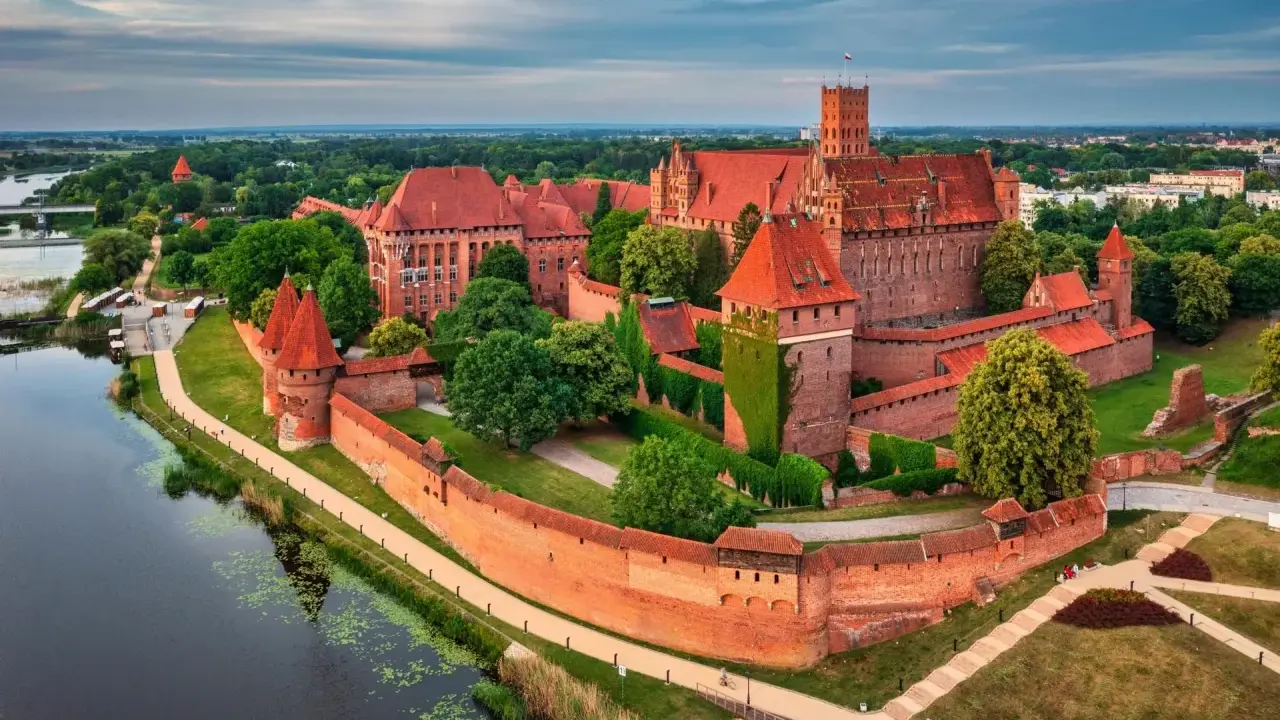 Potężny zamek w Malborku, największy zamek na świecie, otoczony murami obronnymi i rzeką, z czerwonymi dachami i wieżami.