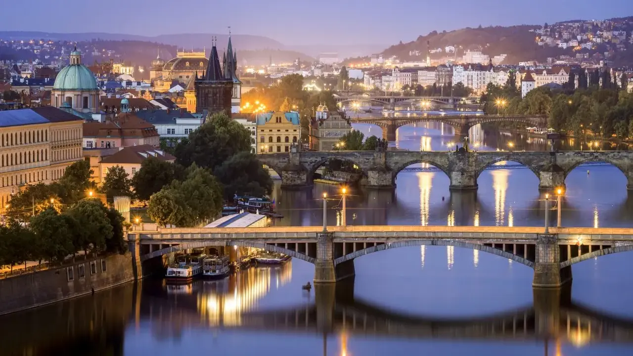 Praga nocą, z licznymi mostami na Wełtawie i oświetlonymi budynkami. Ciekawe ciekawostki o Czechach czekają na odkrycie w tym magicznym mieście.