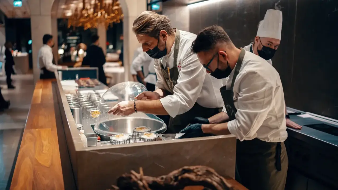 Szefowie kuchni w atelier amaro przygotowują dania. W tle widać eleganckie wnętrze restauracji.