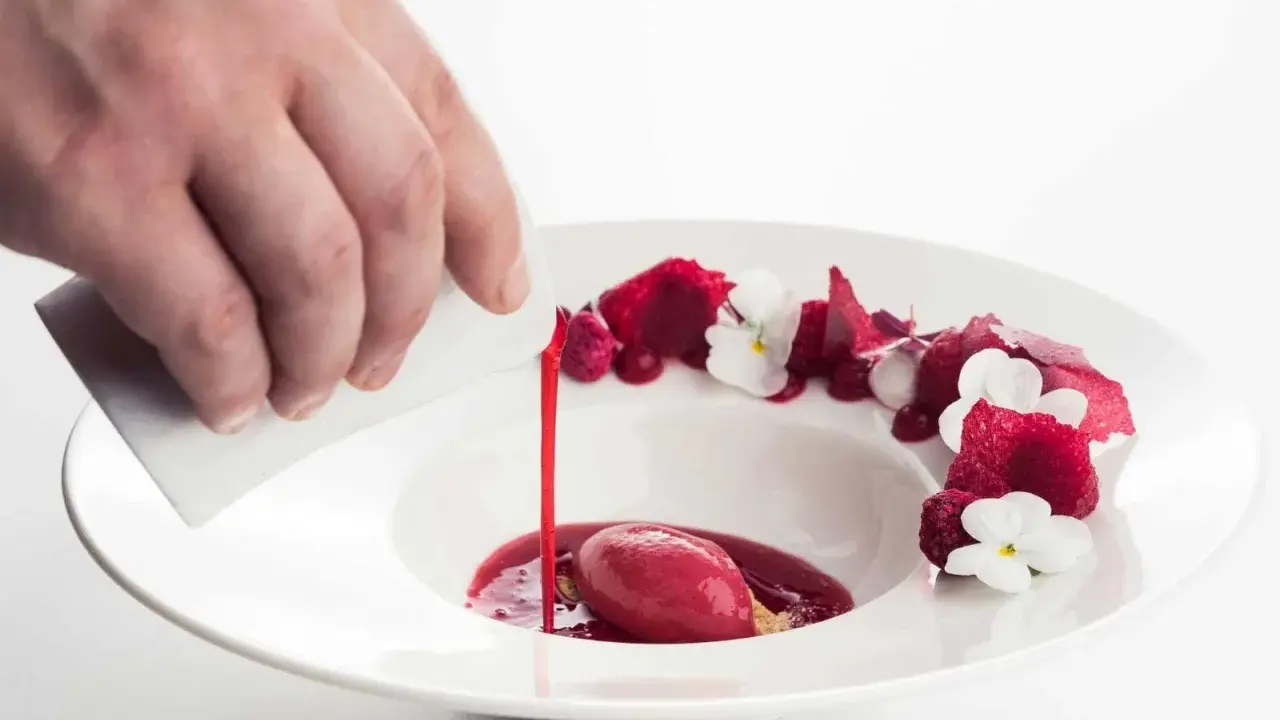 Wykwintny deser w restauracji z gwiazdką Michelin: malinowy sorbet z sosem i jadalnymi kwiatami, polany przez kucharza.