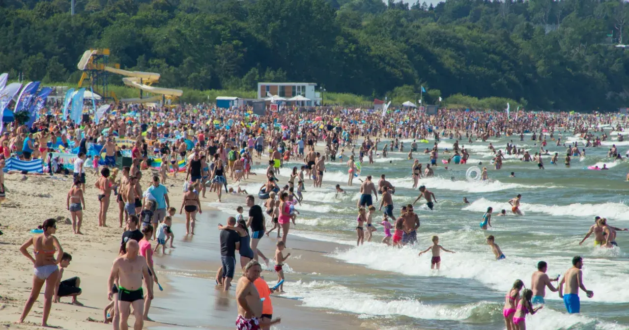Tłumy ludzi na plaży i w wodzie, zjeżdżalnie wodne w tle. Idealne miejsce na wakacje w Polsce!