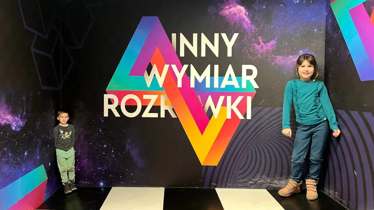 Dzieci w "Innym Wymiarze Rozrywki" w Warszawie. Kolorowa ściana z motywem kosmosu i geometrycznymi kształtami.