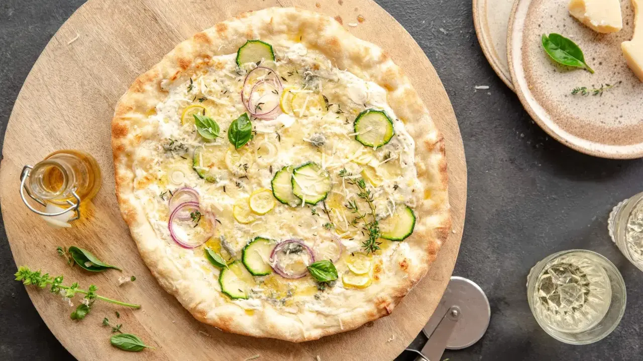 Pyszna pizza bianca z cukinią, cebulą i cytryną, podana na drewnianej desce.