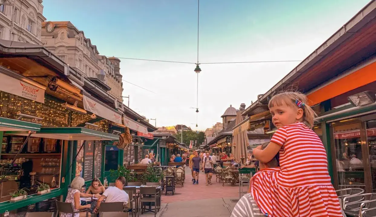 Wiedeń rynek tętni życiem. Dziewczynka na ramionach taty podziwia gwarne uliczki z restauracjami i sklepikami.