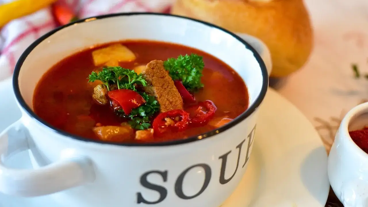 Aromatyczna zupa gulaszowa w białej misce z napisem "SOUP", ozdobiona natką pietruszki i papryką. Idealna na chłodne dni, to jedne z tych **dobrych zup domowych**.