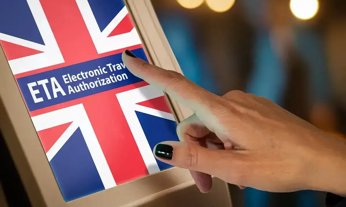 Dłoń dotyka ekranu z flagą Wielkiej Brytanii i napisem "ETA Electronic Travel Authorization". Czy do Londynu trzeba paszport? Sprawdź ETA.