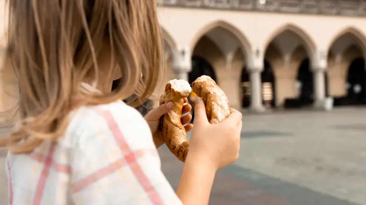Dziecko trzyma obwarzanka na tle Sukiennic. Smaki Krakowa z dzieckiem.