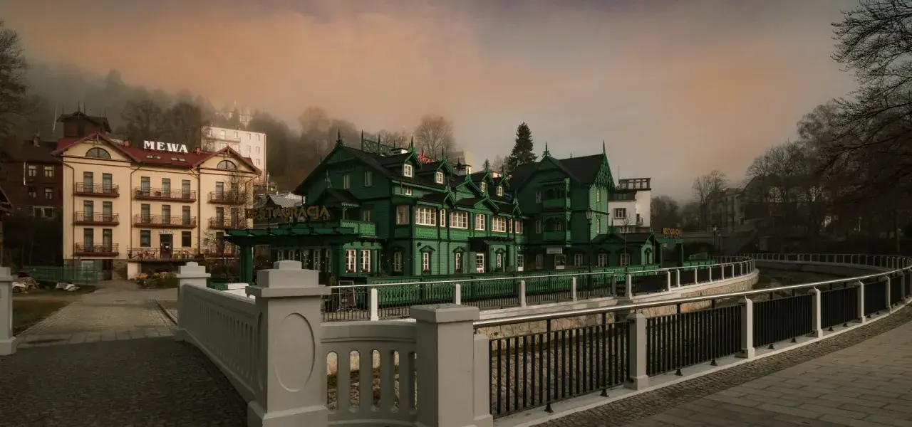 Krynica-Zdrój atrakcje wieczorem: malownicza, zielona willa z restauracją i hotel Mewą w mglistym, jesiennym krajobrazie.