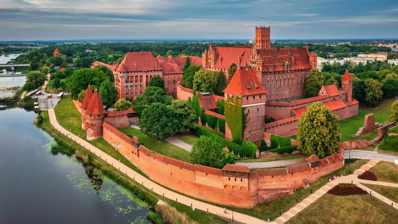 Potężny zamek w Malborku, otoczony murami, z wieżami i zielenią. Ciekawostki o tym miejscu przyciągają turystów.