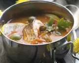 Aromaticzna rosyjska zupa rybna z kawałkami ryby, oliwkami, cytryną i natką pietruszki w metalowej misce.