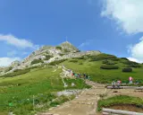 Tłum turystów wspina się kamienistym szlakiem na Giewont. Widać krzyż na szczycie.