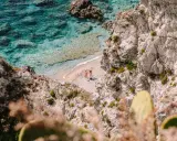 Malownicza zatoczka na Kalabrii, gdzie warto zobaczyć turkusowe morze i skaliste wybrzeże. Dwie osoby odpoczywają na piaszczystej plaży.