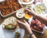 Stół z potrawami do burrito: szarpana wieprzowina, surówka, guacamole i sosy.