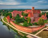 Potężny zamek w Malborku, największy zamek na świecie, otoczony murami obronnymi i rzeką, z czerwonymi dachami i wieżami.