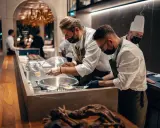 Szefowie kuchni w atelier amaro przygotowują dania. W tle widać eleganckie wnętrze restauracji.