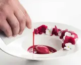 Wykwintny deser w restauracji z gwiazdką Michelin: malinowy sorbet z sosem i jadalnymi kwiatami, polany przez kucharza.