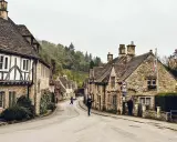 Kamienna uliczka w Cotswolds, z tradycyjnymi domami i drzewami na wzgórzach.