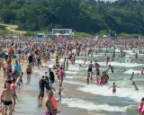 Tłumy ludzi na plaży i w wodzie, zjeżdżalnie wodne w tle. Idealne miejsce na wakacje w Polsce!