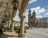 Urokliwe arkady Sukiennic w Krakowie, z widokiem na Kościół Mariacki i tętniący życiem Rynek. Stare miasto w Krakowie zachwyca.