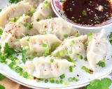Pierożki gyoza, posypane szczypiorkiem i sezamem, podane z sosem.