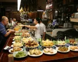 Tapas bar pełen ludzi wybierających przekąski. Na ladzie mnóstwo małych kanapeczek i innych przysmaków.