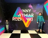 Dzieci w "Innym Wymiarze Rozrywki" w Warszawie. Kolorowa ściana z motywem kosmosu i geometrycznymi kształtami.