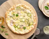 Pyszna pizza bianca z cukinią, cebulą i cytryną, podana na drewnianej desce.