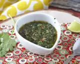 Aromaticzny sos chimichurri w białej miseczce, obok ćwiartka limonki i świeża kolendra. Idealny do grillowanych mięs.