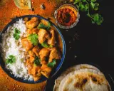 Aksamitny kurczak w sosie butter masala, podany z ryżem i chlebkami naan. Obok miseczka z przyprawami.