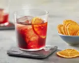 Klasyczny negroni przepis: czerwony koktajl z lodem i plasterkiem pomarańczy, obok miseczka suszonych pomarańczy.