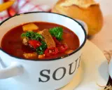 Aromatyczna zupa gulaszowa w białej misce z napisem "SOUP", ozdobiona natką pietruszki i papryką. Idealna na chłodne dni, to jedne z tych **dobrych zup domowych**.