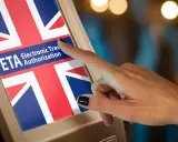 Dłoń dotyka ekranu z flagą Wielkiej Brytanii i napisem "ETA Electronic Travel Authorization". Czy do Londynu trzeba paszport? Sprawdź ETA.