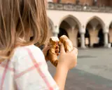 Dziecko trzyma obwarzanka na tle Sukiennic. Smaki Krakowa z dzieckiem.
