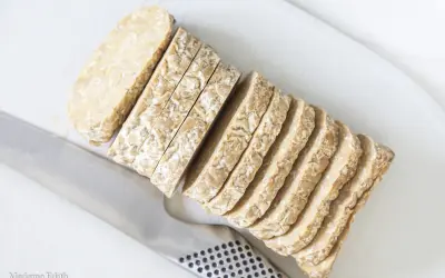 Pokrojony w plastry tempeh, czyli fermentowana soja, leży obok noża. To świetny składnik do wegańskich potraw.