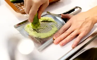 Ręka trze korzeń wasabi o tarkę. To właśnie tak powstaje świeże wasabi, które dodaje ostrości potrawom.