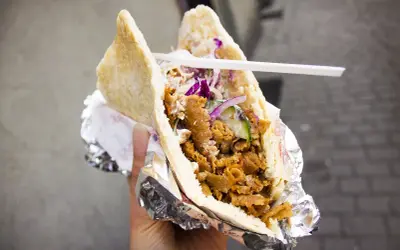 Pyszny kebab w bułce z mięsem, warzywami i sosem. To danie, które swoją popularność zawdzięcza podróżom i wymianie kulturowej, pokazując skąd pochodzi kebab.