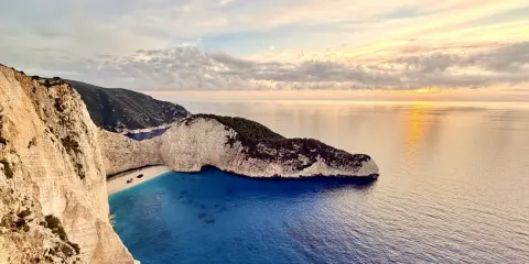Zachód słońca nad Navagio, słynną zatoką wraku na Zakynthos. Białe klify, turkusowa woda i wrak statku tworzą malowniczy krajobraz.