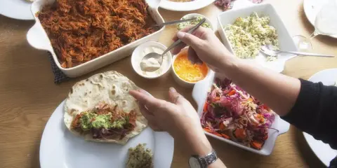 Stół z potrawami do burrito: szarpana wieprzowina, surówka, guacamole i sosy.