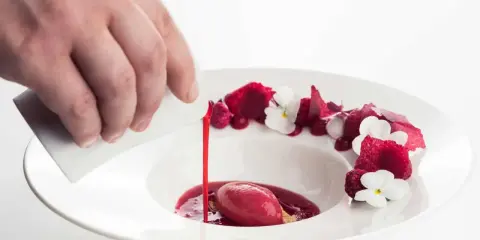Wykwintny deser w restauracji z gwiazdką Michelin: malinowy sorbet z sosem i jadalnymi kwiatami, polany przez kucharza.