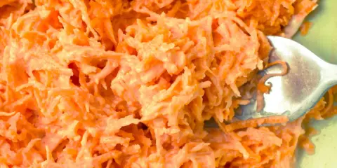 Pyszna surówka z marchewki jak z restauracji, kremowa i apetyczna. Widoczna łyżka widelca zagłębiająca się w jej wnętrze.
