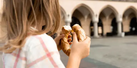 Dziecko trzyma obwarzanka na tle Sukiennic. Smaki Krakowa z dzieckiem.
