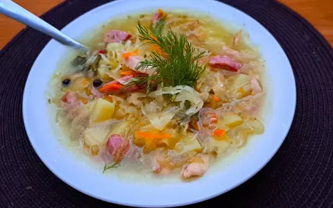 Syta zupa z kiszonej kapusty z ziemniakami i kiełbasą, ozdobiona koperkiem. Pyszne dania z kapusty na zimowe wieczory.