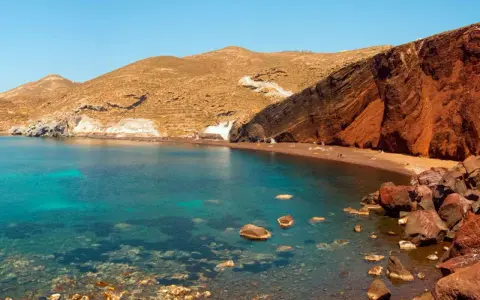 Santorini plaże: Czerwona plaża z turkusową wodą i skalistymi klifami.