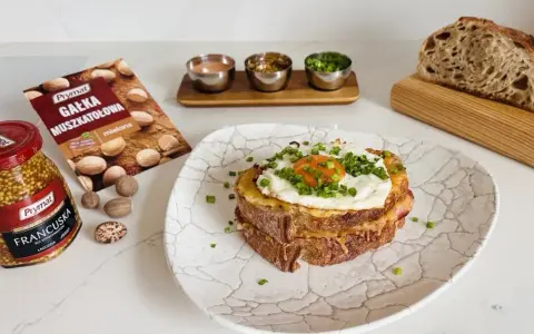 Pyszny croque madame z jajkiem sadzonym i szczypiorkiem, obok musztarda francuska i gałka muszkatołowa.