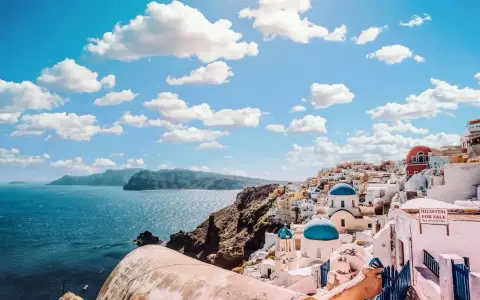 Santorini, Grecja. Białe domy z niebieskimi kopułami kościołów na zboczu góry, widok na morze. Zastanawiasz się, ile się leci do Grecji?