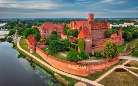 Potężny zamek w Malborku, największy zamek na świecie, otoczony murami obronnymi i rzeką, z czerwonymi dachami i wieżami.