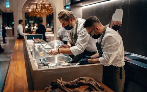 Szefowie kuchni w atelier amaro przygotowują dania. W tle widać eleganckie wnętrze restauracji.